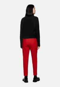 Schwarzer Strickpullover mit strukturiertem Rücken, kombiniert mit schlanken roten Hosen und schwarzen klobigen Stiefeln, von hinten betrachtet.
