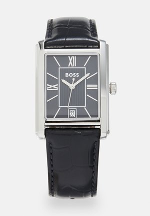 Square silver watch with a black crocodile leather strap. Black dial features Roman numerals, vertical lines, and a date display at 6 o'clock.