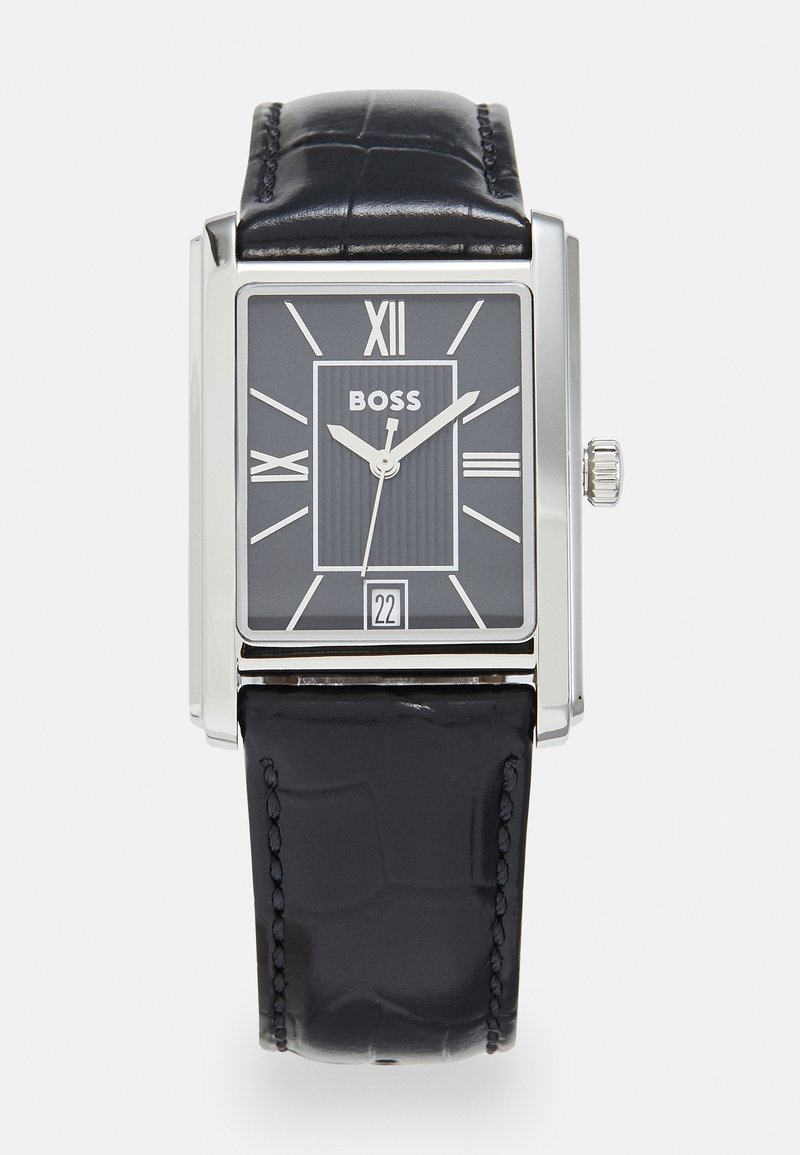 Montre carrée en argent avec un bracelet en cuir de crocodile noir. Le cadran noir présente des chiffres romains, des lignes verticales et un affichage de la date à 6 heures.