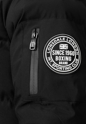 Giubbotto imbottito nero con un patch del logo ricamato sul braccio superiore, una tasca con zip e una finitura liscia e opaca.