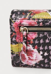 Carteira em material sintético preto com padrão floral, equipada com zíper dourado e detalhes em dourado, apresentando rosas cor-de-rosa e verdes sobre uma superfície texturizada.