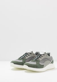 Scarpe da ginnastica verdi e grigie realizzate in suede e materiali sintetici, con dettagli testurizzati e una suola bianca ammortizzata.