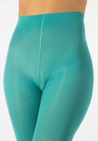 Leggings turchesi realizzati in un tessuto elastico e liscio. Presentano una cintura in vita e una cucitura che corre lungo la parte frontale, con un design affusolato.