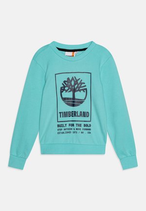 Sweatshirt turquoise à manches longues, col rond et poignets côtelés. Présente un logo d'arbre noir et du texte imprimé sur le devant.
