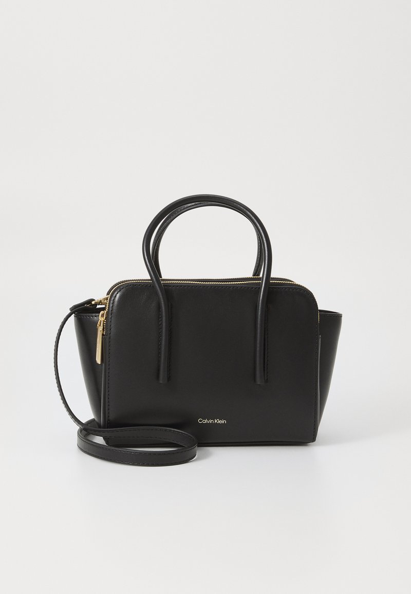Bolsa de mão em pele preta com fecho em metal dourado, duas alças superiores e uma alça de ombro destacável. Apresenta um logótipo discreto na parte da frente.