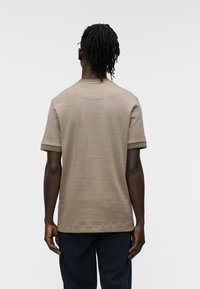 Μπλουζάκι με κοντά μανίκια σε μπεζ χρώμα, με στρογγυλή λαιμόκοψη και ριμπ μανσέτες. Διαθέτει υφή υφάσματος και διακριτική λεπτομέρεια λογότυπου στο πίσω μέρος του λαιμού.