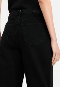 Mustad denim teksad kõrge vöökoht, sirge jala disain; sisaldab kahte tagakotti ja bränditud vöö sildiga. Sile tekstuur.