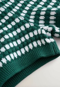 Tissu tricoté vert avec motif géométrique de points blancs et bord côtelé, montrant les détails de texture et de pli.