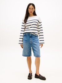 Camisa de mangas longas às riscas em creme e azul-marinho, combinada com calções de ganga azuis e mocassins castanhos brilhantes. Design simples com um corte descontraído.