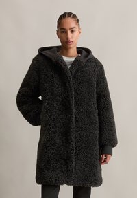 Zwarte fleece jas met een gestructureerde, fluffy buitenkant, voorzien van een grijze capuchon, lange mouwen en een rechte silhuet. Minimalistische ontwerpdetails.