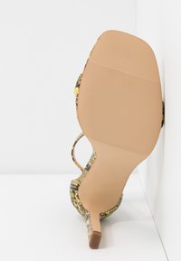 Sandał na wysokim obcasie z teksturowaną, wielokolorową cholewką w wzór skóry węża. Podeszwa w kolorze jasnobrązowym z rowkowanymi detalami.