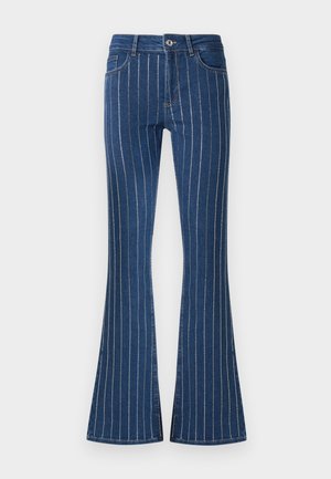 Mėlynos džinsinės kelnės su plačiu apatiniu kraštu, turinčios vertikalias baltas juosteles, užtrauktuką ir priekinėmis kišenėmis. Audinys šiek tiek tekstūruotas.