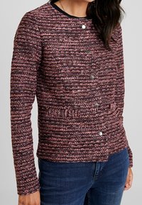 Gelaagd, gemêleerd stoffen jasje met een ronde halslijn, zes knoopsluitingen en twee voorkanten met horizontale details.