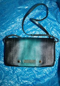 Zwarte en teal gestructureerde schoudertas met metallic accenten en een klep sluiting. Beschikt over een lange verstelbare schouderriem en een patroon detail aan de voorkant.