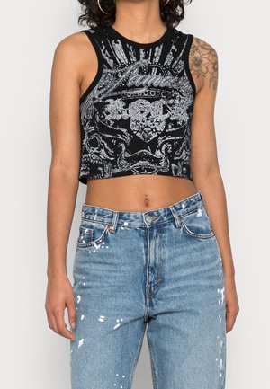 Zwart cropped tanktop met zilveren grafisch ontwerp met sierlijke patronen. Gecombineerd met blauwe hoge taille jeans met witte verfspatten.