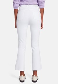 Jean flare blanc avec une finition brute, en denim. Comprend une taille haute, deux poches arrière et un design minimaliste.