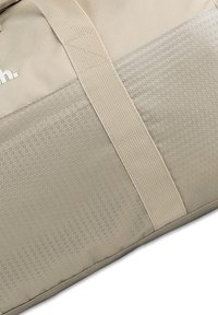 Beige sporttas met een honingraatpatroon, gestructureerd oppervlak en stevige handvaten. Logo afgedrukt aan de zijkant.