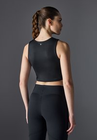 Top corto negro sin mangas hecho de material suave, con cuello redondo y un pequeño detalle de logo en la parte posterior; combinado con leggings negros de cintura alta.
