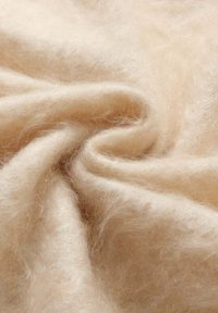 Tessuto di colore crema, morbido al tatto e con una texture pelosa, che mostra una piega a spirale e giochi di luce tra le fibre, suggerendo calore e accoglienza.