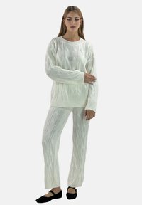 Hvid strikket sweater og matchende bukser med et kabelstrikkemønster; begge har en afslappet pasform og ribbede manchetter og kant.