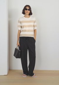 Haut en tricot beige et blanc rayé avec des manches courtes, associé à un pantalon noir ample. Accessoirisé avec un petit sac à main noir et des lunettes de soleil.