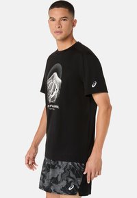 Sort atletik t-shirt med et hvidt bjergmotiv og tekst, kombineret med mønstrede sorte shorts med bølgemønstre.