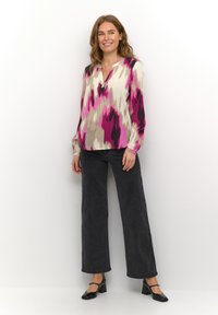Langdurige blouse met een veelkleurig abstract patroon in roze, grijs en crème. Gepaarde met zwarte wijde broek en zwarte hoge hakken.