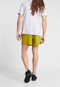 Grüne, leichte Shorts, ein lockeres graues T-Shirt und schwarze Sportschuhe. Sichtbarer strukturierter Stoff und seitliche Schlitze an den Shorts.