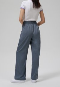 Lätta, grå avslappnade byxor med elastisk midja och sidofickor, i kombination med en vit topp med lila kant, och vita sneakers.