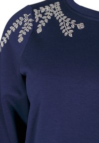 Marinblå tröja i mjukt tyg, med silverfärgade bladsyningsbroderier på axlarna för extra textur och detalj.