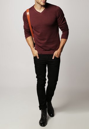 Bordeauxrode gebreide trui met v-hals en geribbelde manchetten, gecombineerd met strakke zwarte jeans en zwarte leren enkellaarzen, aangevuld met een bruine band.