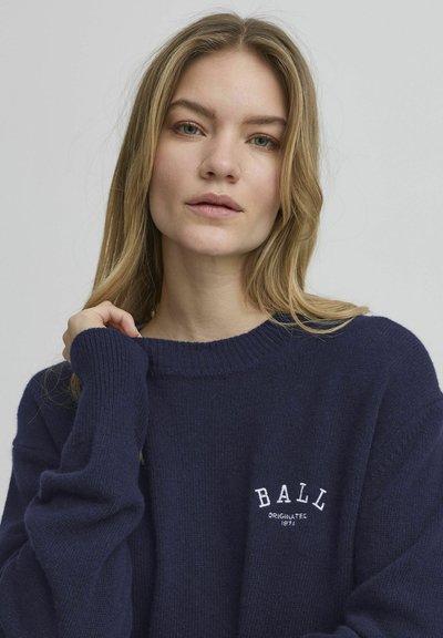 Mørkeblå strikkegenser med rund hals og lange ermer. Har hvit brodert tekst "BALL" og "ORIGINERT 1976" på brystet.