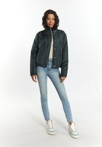 Giacca cropped nera in piuma con colletto alto, indossata sopra una maglietta a righe. Jeans azzurri chiari e sneaker multicolori completano il look.