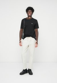 Black t-shirt with small logo, cream-colored pants, and black shoes. Simple design, fitted shape, and smooth texture. Black shoulder bag.