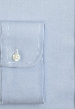 Světlomodrý manžetový košile s bílým knoflíkem a viditelným šitím na hladkém textilním pozadí.