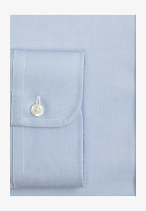 Poignet de chemise bleu clair avec un bouton blanc et des coutures visibles sur un fond de tissu lisse.