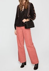Black blouse with embroidered accents, paired with pink wide-leg corduroy pants. Black handbag and ankle boots complete the outfit.