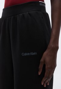 Czarne spodnie dresowe z elastycznym pasem i wyhaftowanym logo Calvin Klein w jasnoniebieskim kolorze. Gładka faktura i luźny krój.