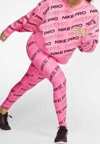 Il sudore e i leggings Nike Pro rosa presentano un audace marchio nero. I materiali sono lisci ed elasticizzati, offrendo un design atletico aderente.