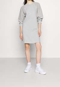 Robe sweatshirt grise avec texture matelassée sur les manches, poignet côtelé et coupe décontractée, associée à des baskets blanches sportives et des chaussettes.