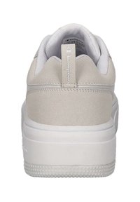 Sneaker bianco con tallone in suede beige testurizzato, intersuola bianca liscia e suola a puntini rialzati. Presenta un'etichetta con il marchio sul retro.