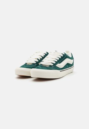 Zapatillas de ante verde con cordones blancos y rayas laterales. Cuentan con una puntera redondeada y una suela de goma texturizada. Diseño minimalista.