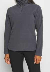 Fleece-pullover i mörkgrått med hög krage, halvmångdragning och två sidofickor. Har långa ärmar och en mjuk textur.