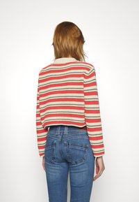 Gestreifter, verkürzter Pullover aus beigefarbenem, korallenfarbenem und grauem Garn mit langen Ärmeln und einem gerippten Ausschnitt, kombiniert mit hochgeschnittenen blauen Jeans.