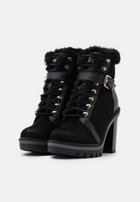 Černé kotníkové boty kombinující semiš a kůži. Mají umělou kožešinu na okraji, zlaté očky a masivní vysoký podpatek pro zvýšení výšky.