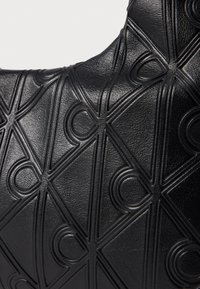 Crna kožna torba s teksturiranom površinom, ukrašenom geometrijskim reljefnim uzorcima i zakrivljenim akcentima raspoređenim u obliku dijamanta.