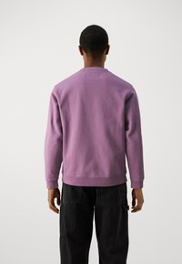 Fioletowa sweatshirt z okrągłym dekoltem i długimi rękawami, wykonana z miękkiego materiału. Widok z tyłu pokazuje luźny krój i ściągacze przy mankietach.