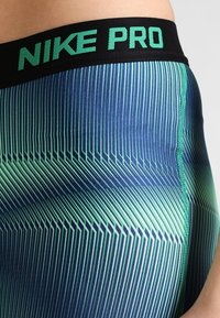 Les shorts Nike Pro présentent une base navy avec des rayures diagonales vertes, une taille noire avec du texte vert et un matériau lisse et extensible.