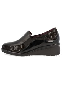 Zapatos negros tipo slip-on con punta de cuero liso y parte superior de tela texturizada con patrones y acentos metálicos; suela de cuña de goma.