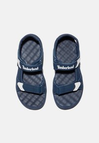 Tummansiniset sandaalit säädettävillä hihnoilla, teksturoitu sisäpohja, valkoiset yksityiskohdat ja pehmustettu kanta mukavuutta varten. Timberland-logo hihnoissa.